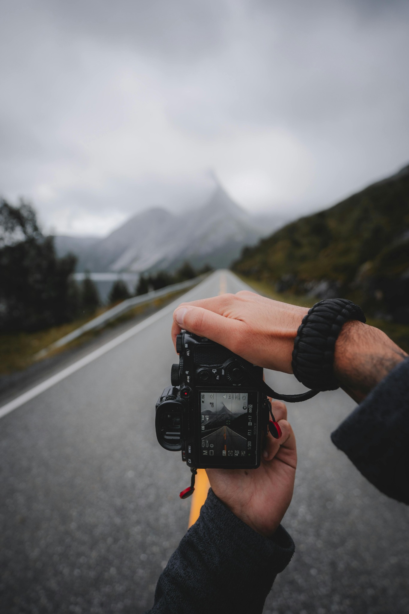 Person wearing a cord bracelet while holding a camera on a mountain road